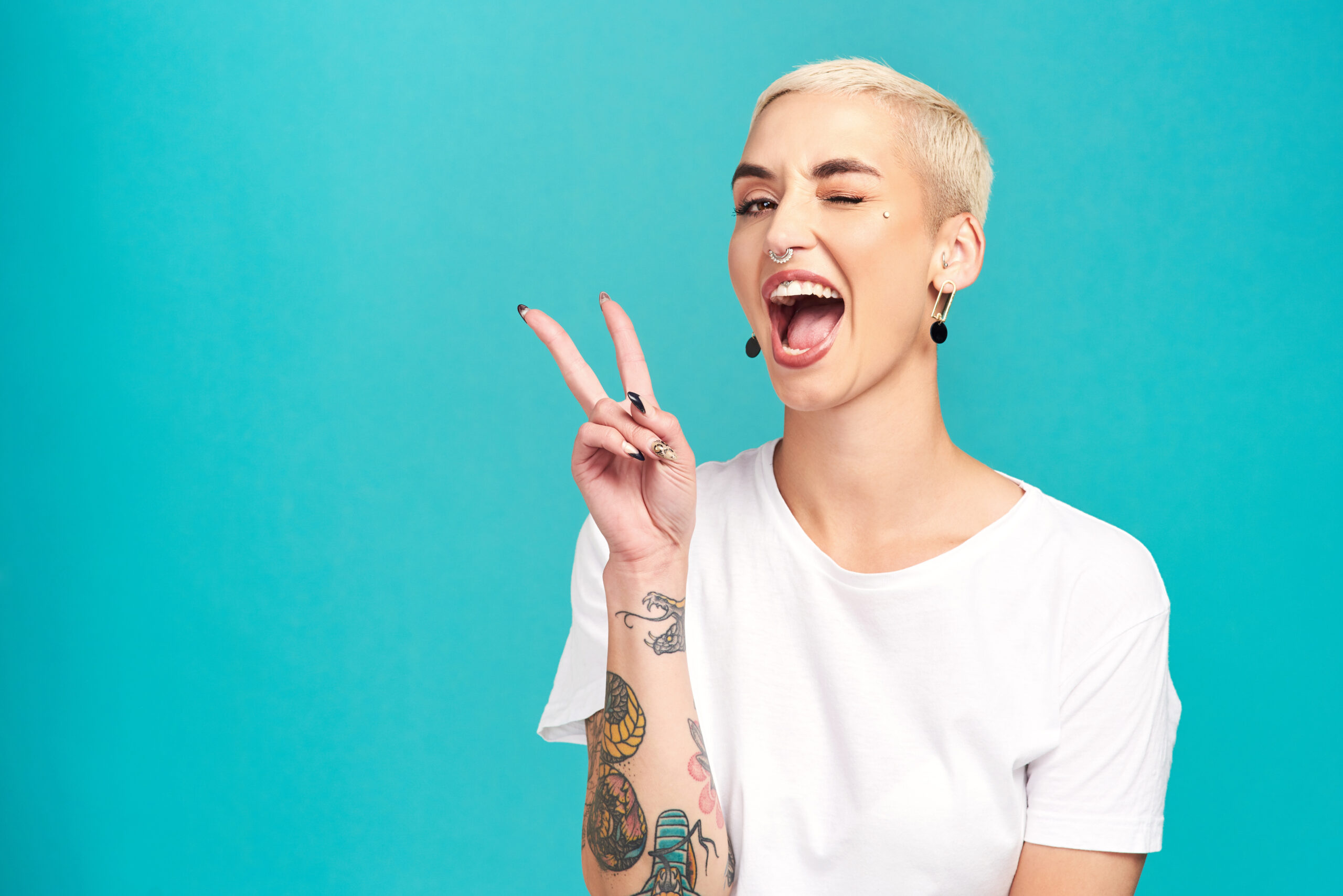 A woman with tattoos making a peace sign on a blue background.